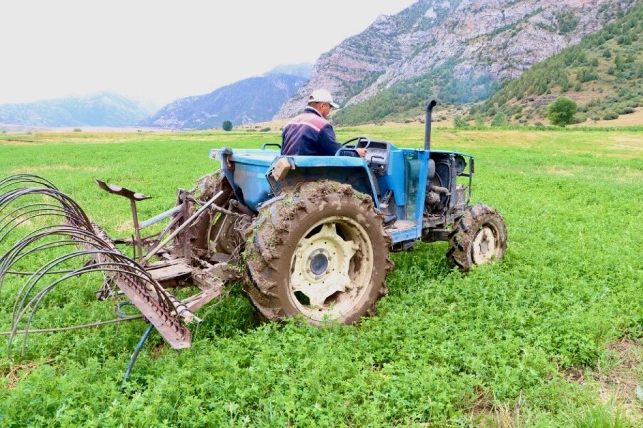 A farmer drives a tractor through a green field backdropped by mountains. Photo: WFP/ Gulnur Cholponbaeva